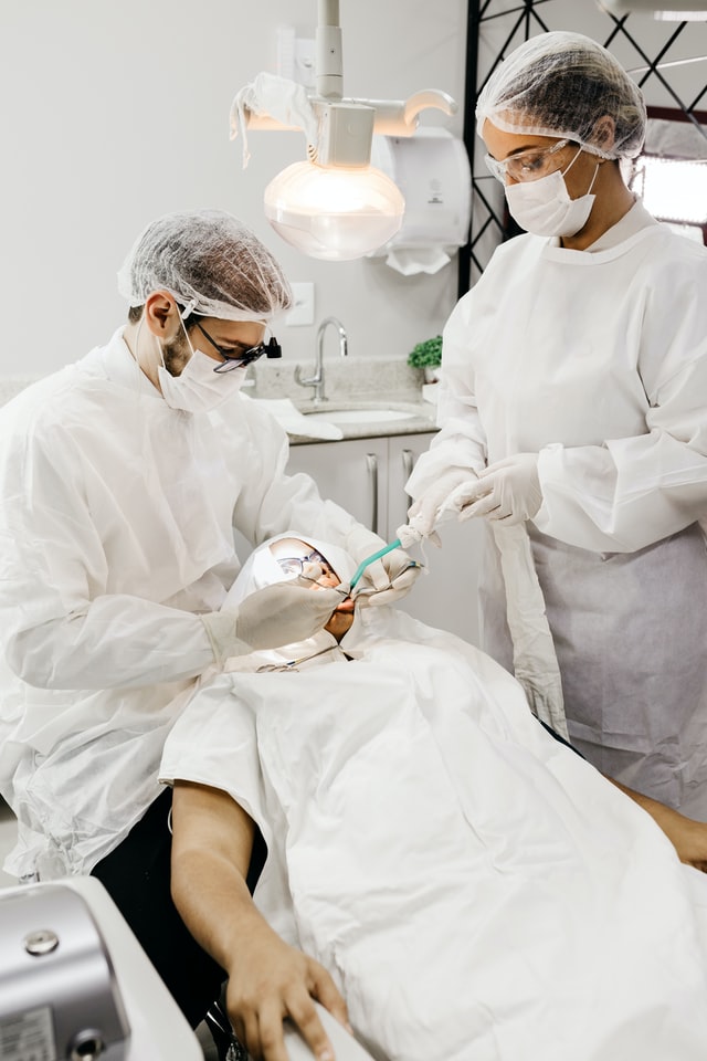dental assistant doing suction as the dentist examines patient