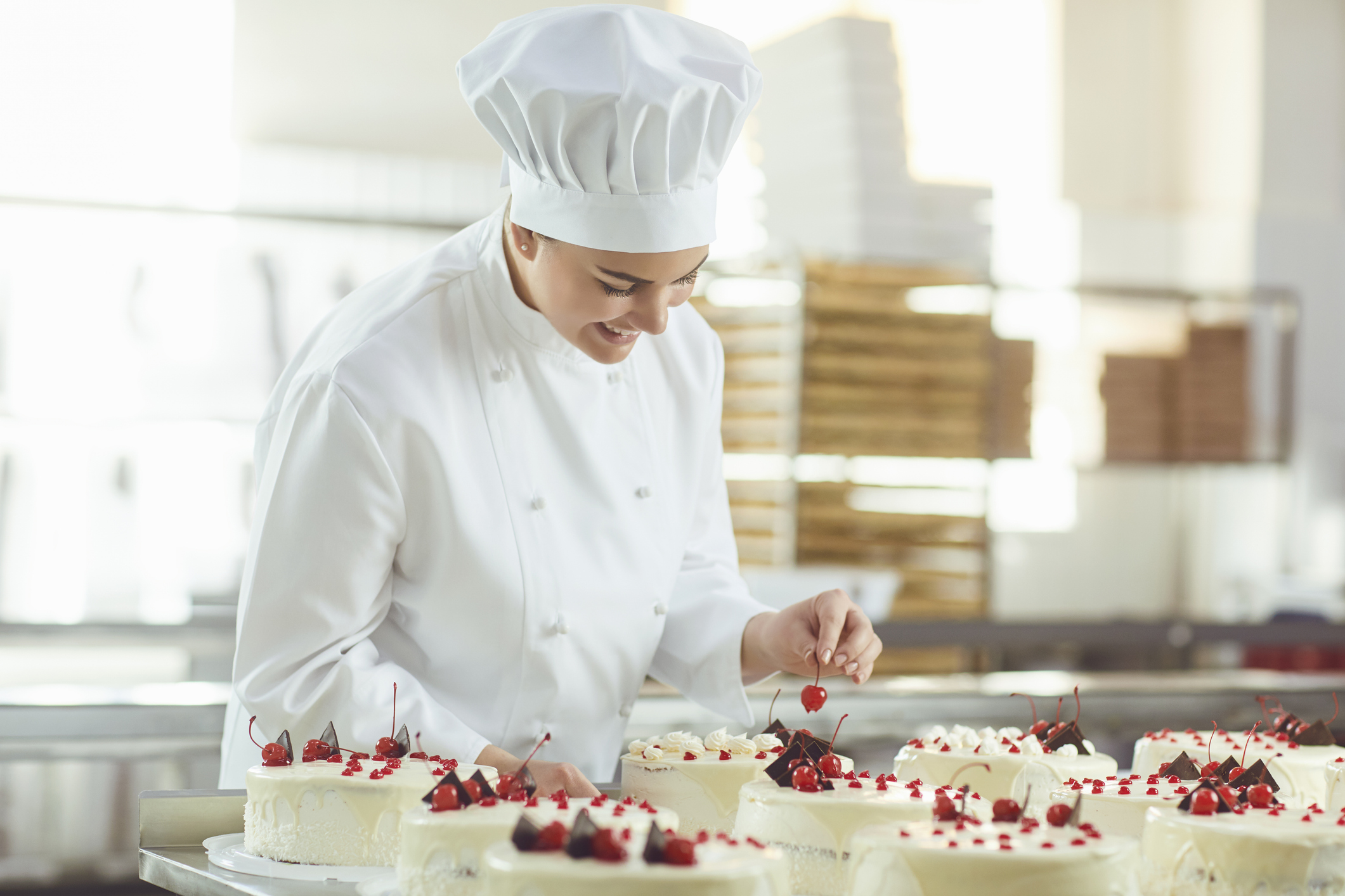 Confectioner is holding a cake in her hand in the bakery.