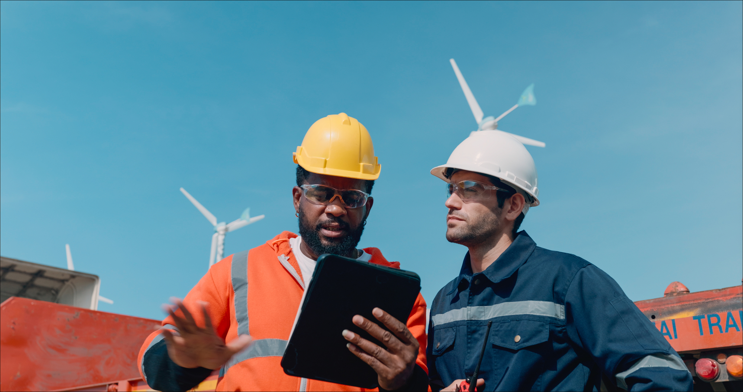 Two Professional Male Managers Wearing Hard Hats Check Inventory and Orders, delivering goods via Airfreight, Seafreight, and inland transit to customers via an application on a digital tablet. Employees work in a distribution center in the logist