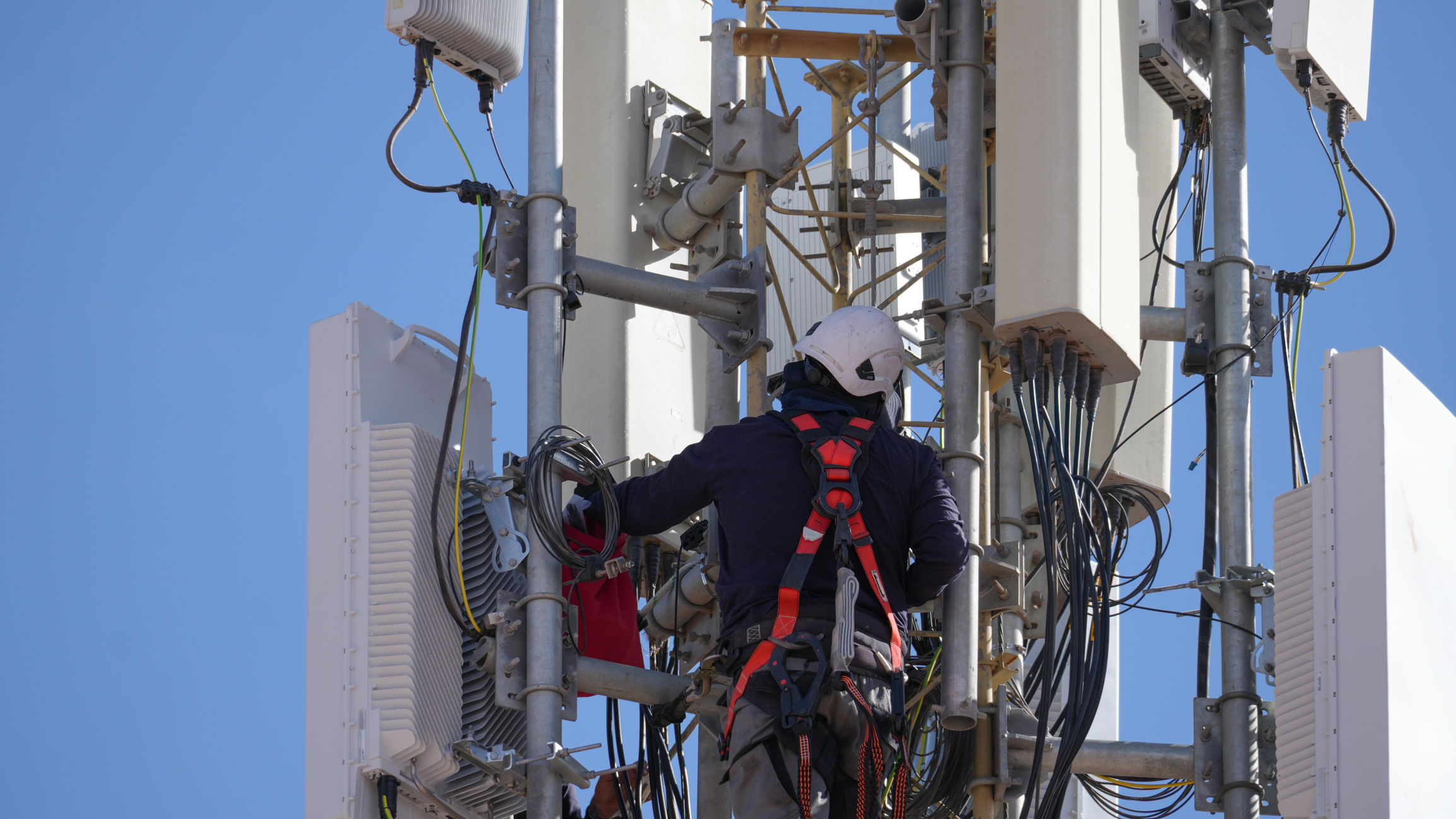 Technician checking equipment and cables on a modern mobile network antenna, providing high-speed connectivity